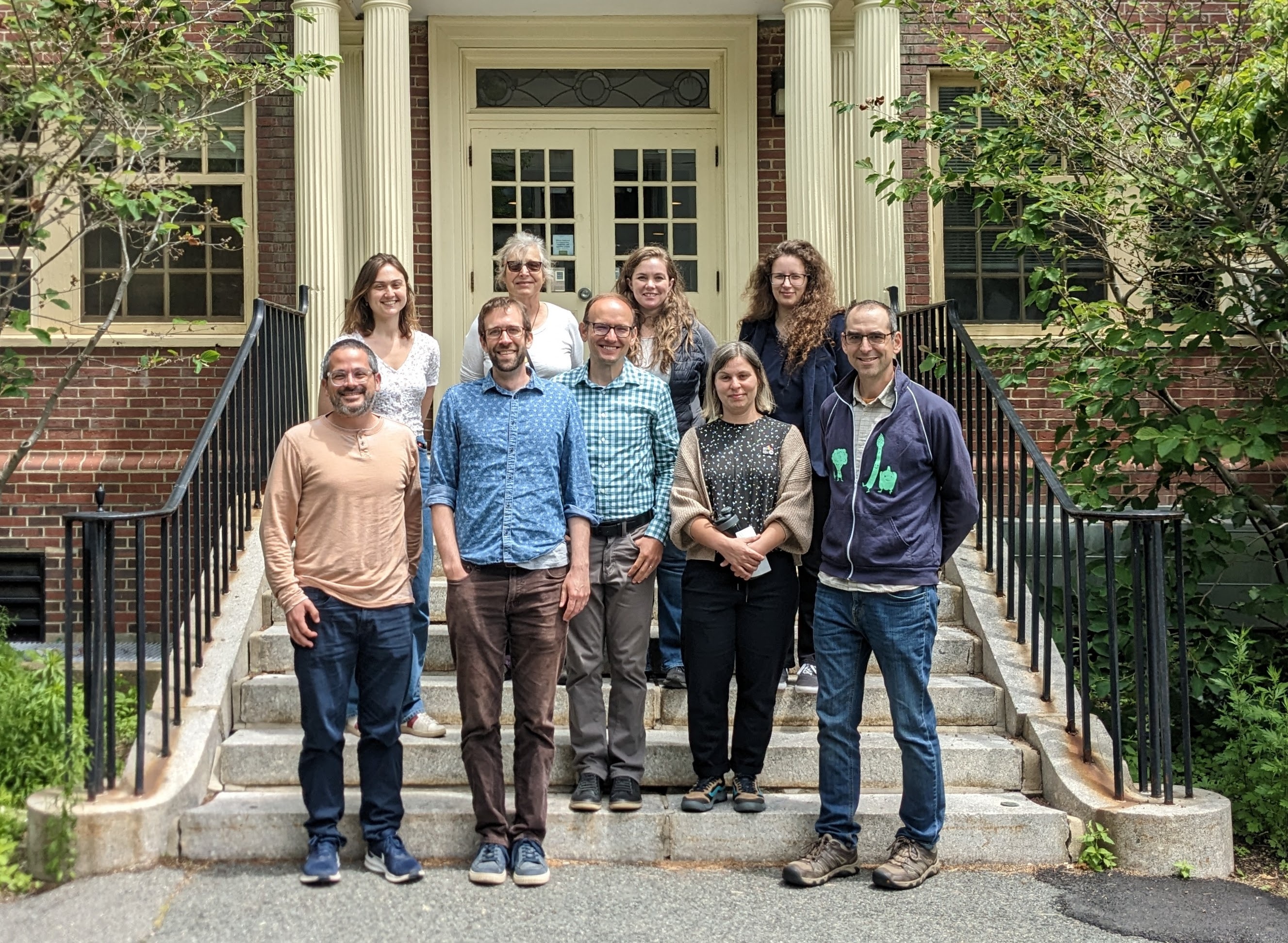 Photo of nine smiling people standing on stairs leading to the front entrance to a building.
