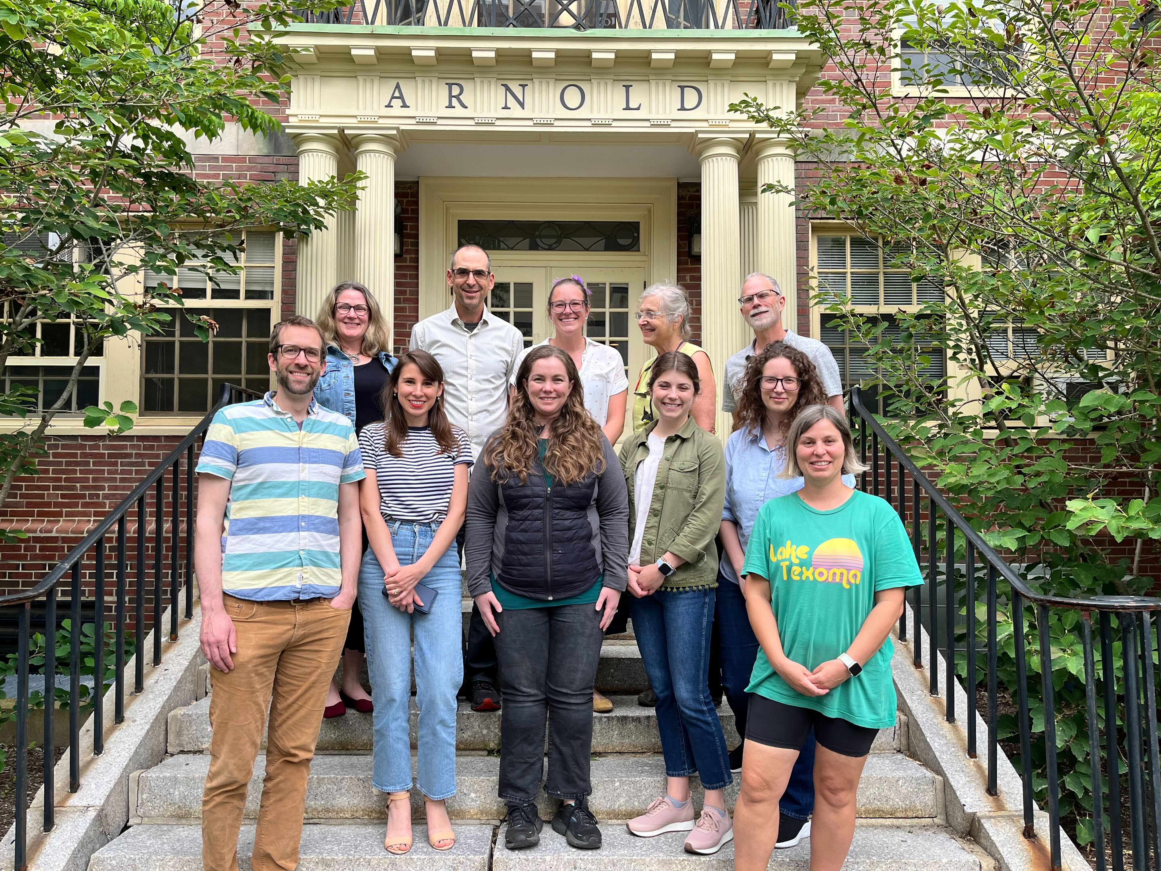 Photo of eleven smiling people standing on stairs leading to the front entrance to a building called Arnold.